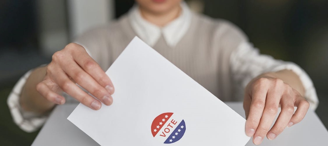 photo of a hand placing a ballot into a box opening